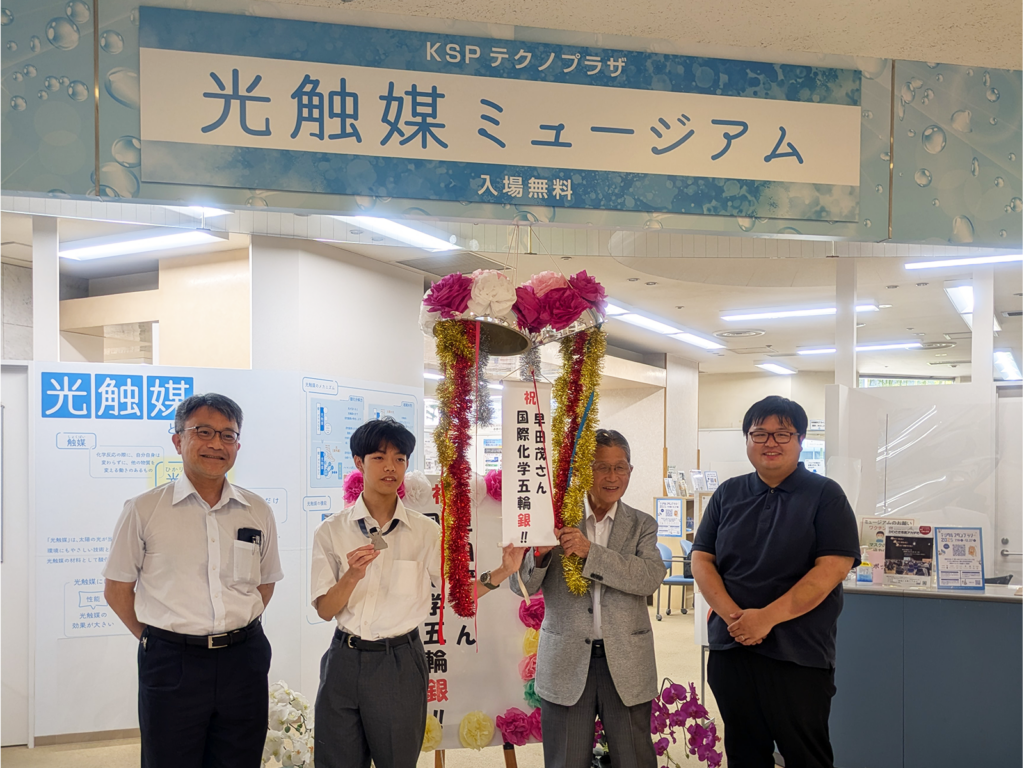 左から落合グループリーダー、銀メダルを手に持った早田さん、藤嶋先生、濱田研究員と、割れたくす玉との記念写真